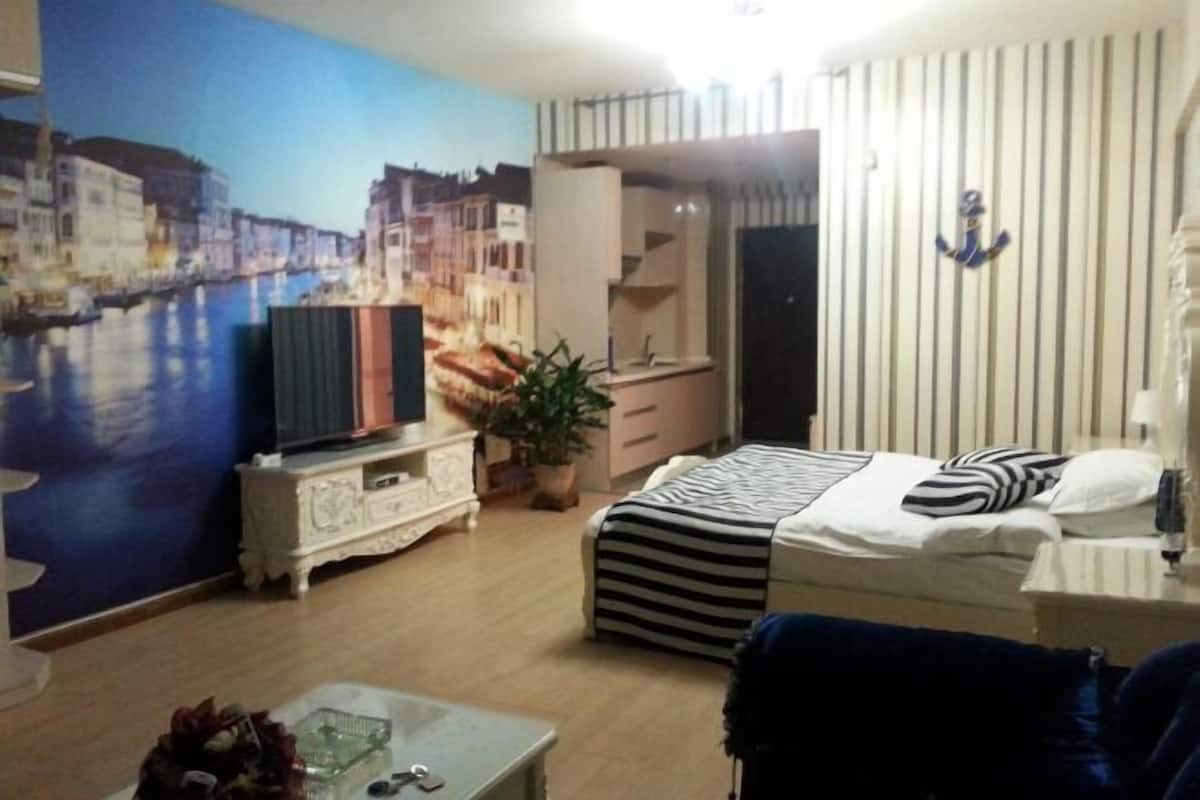 A room with a bed, a TV, a dresser, and a wall with a mural.