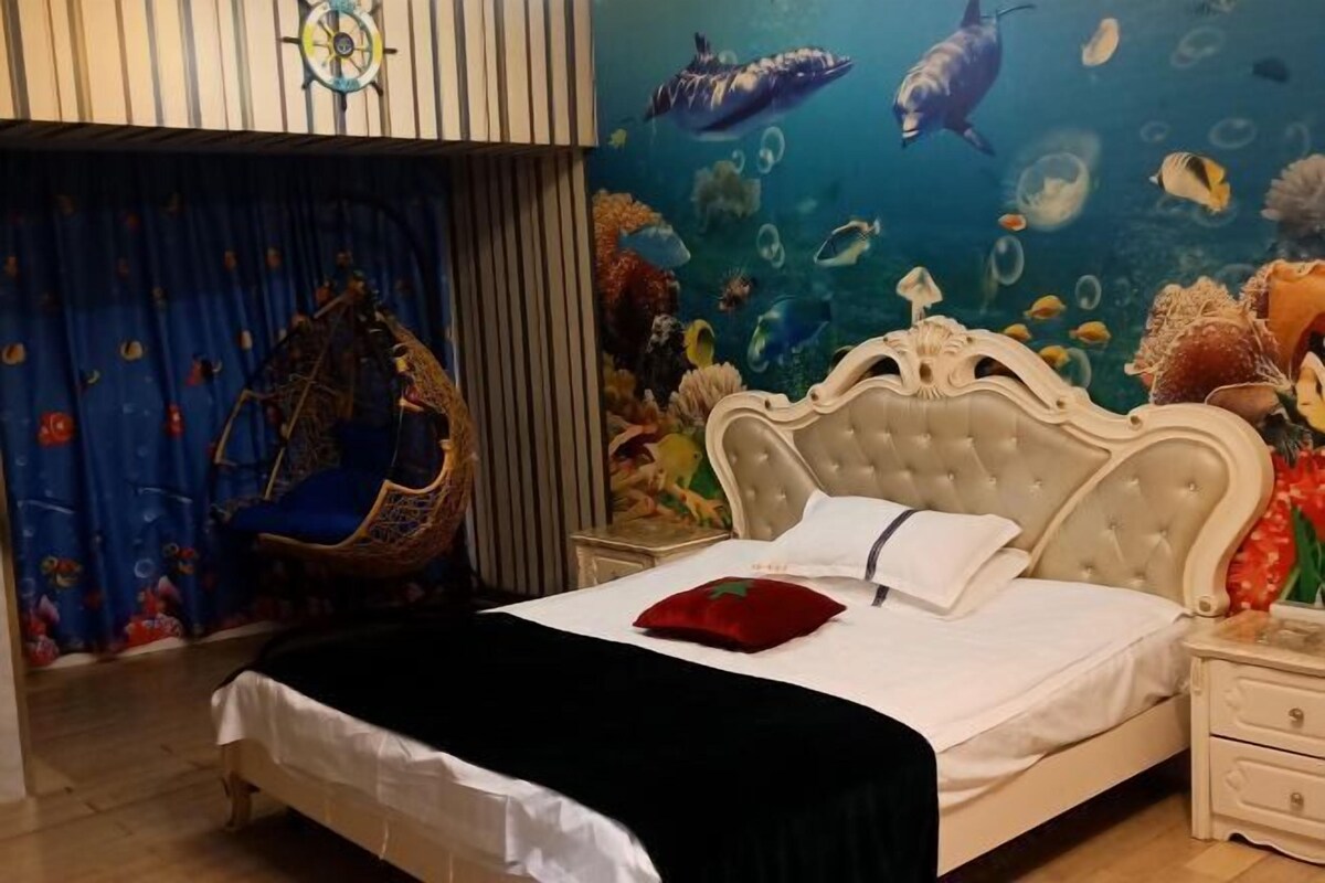 A bedroom with a bed, a nightstand, a chair, and an ocean-themed wall mural.