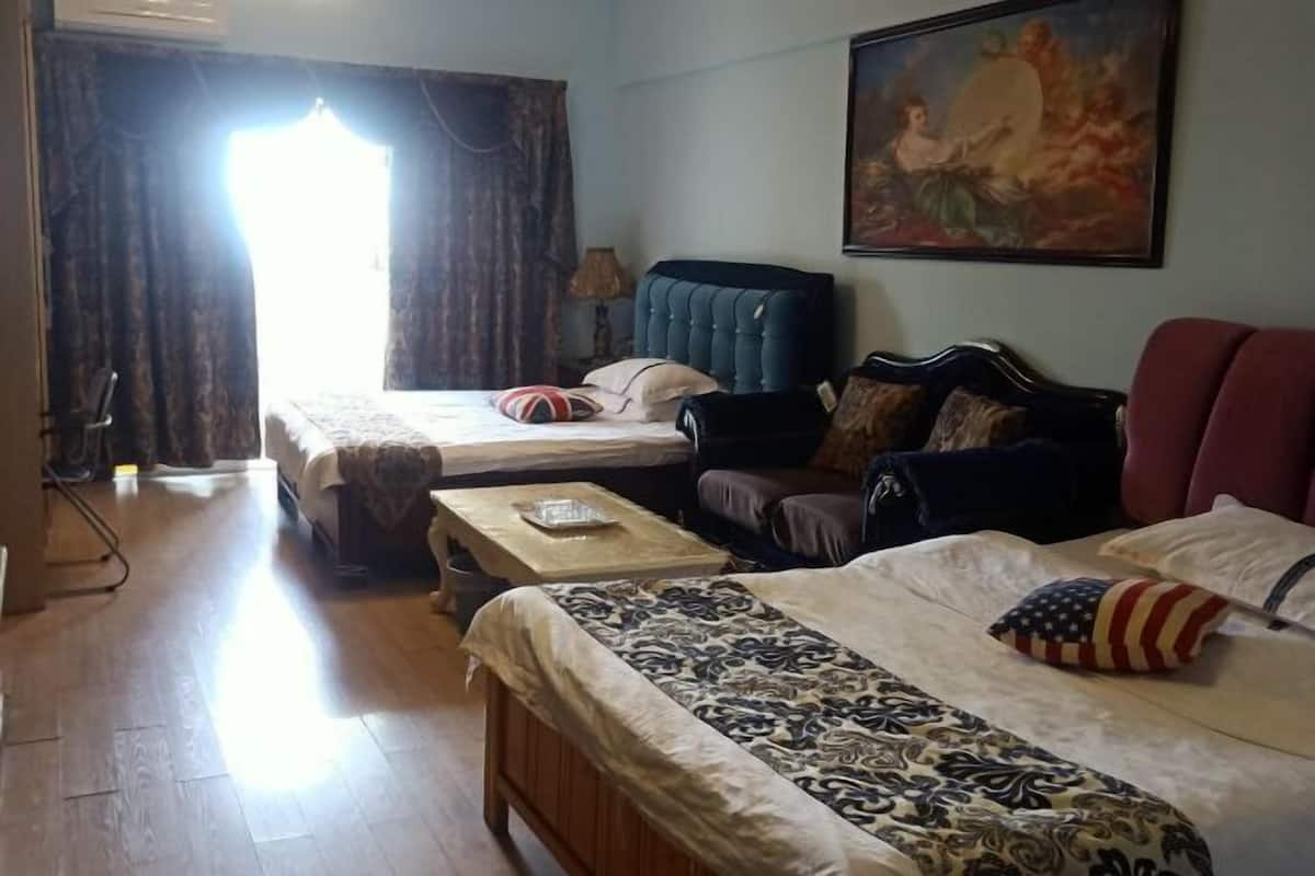 A room with two beds, a sofa, a table, and a painting on the wall.