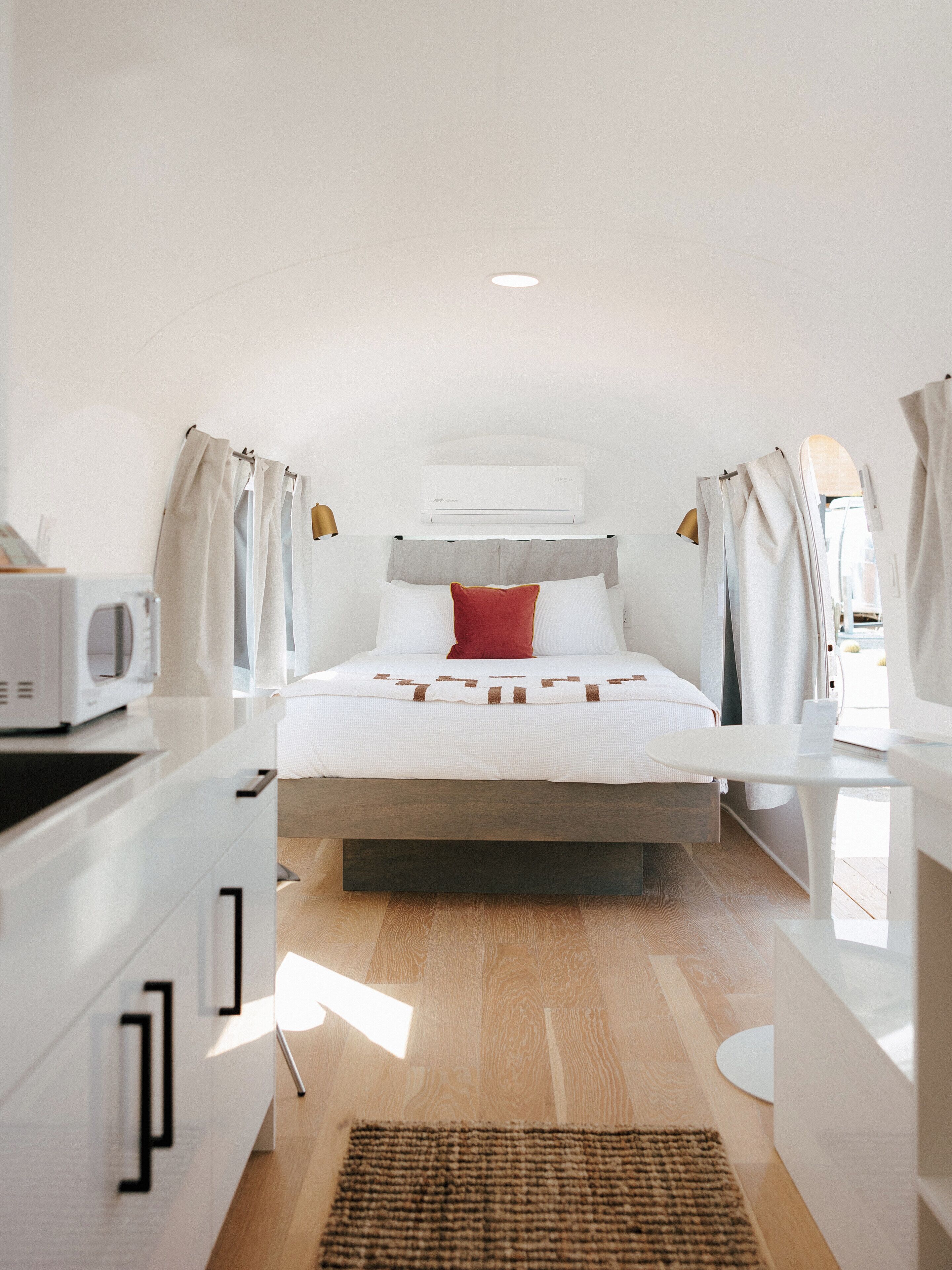 Un dormitorio con cama, mesita de noche, microondas y ventana con cortinas.
