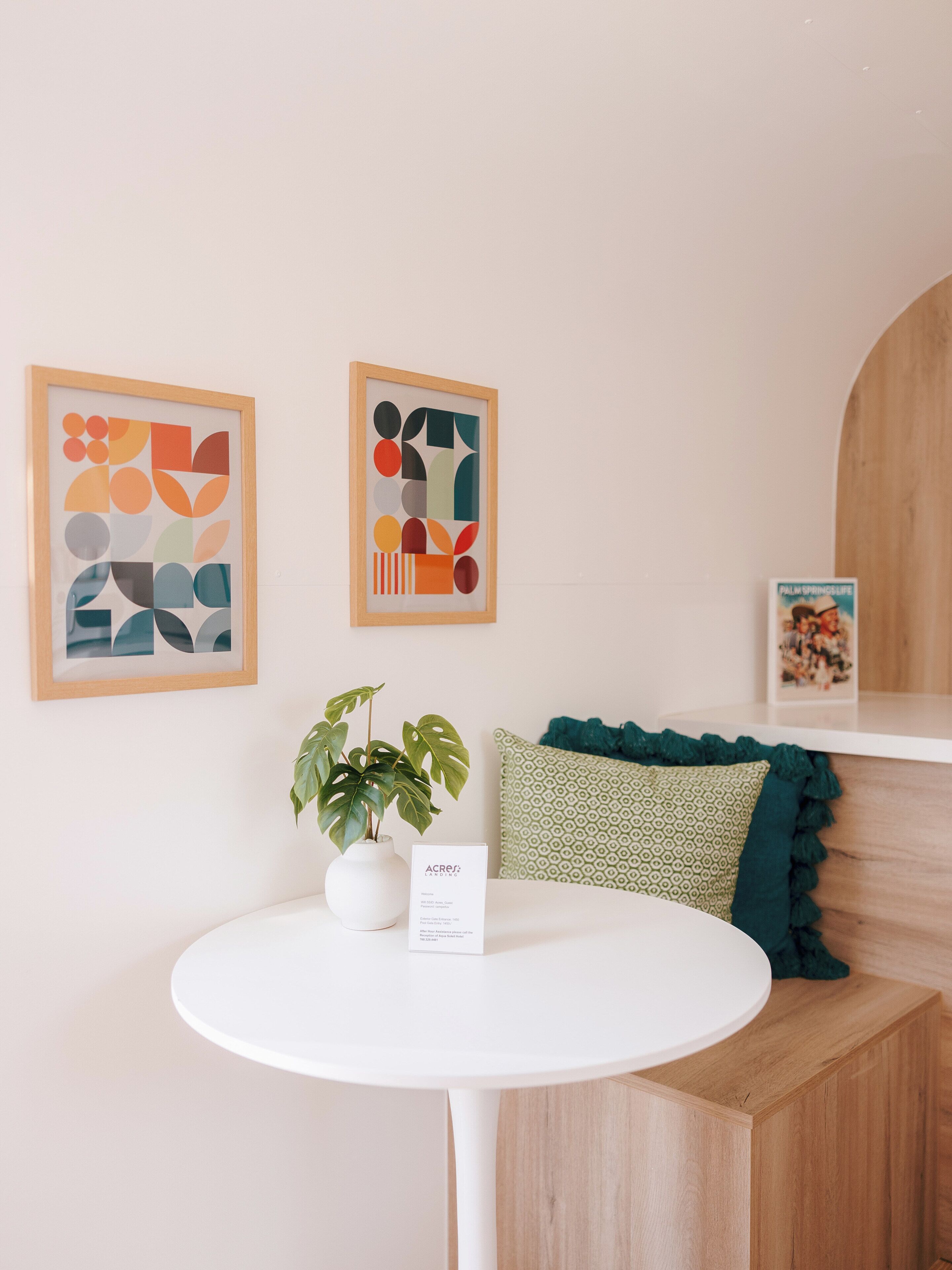 A room with a round white table, a potted plant, and two abstract artworks on the wall.