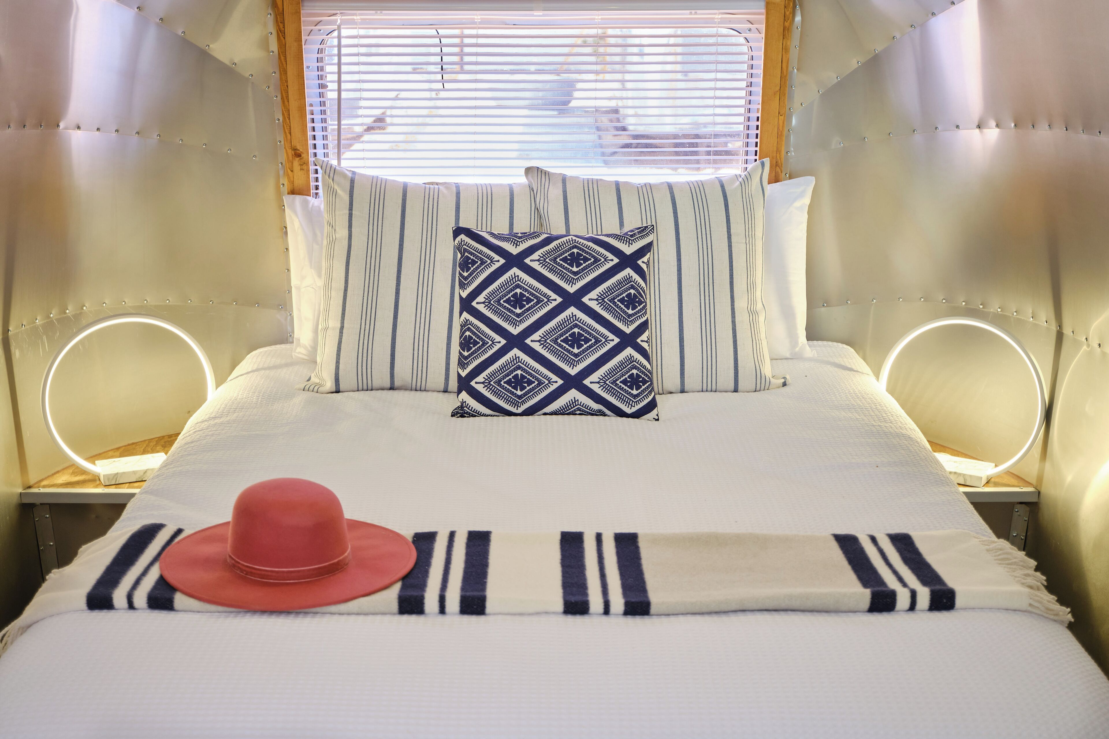 A bed with a patterned pillow, a red hat, and a striped blanket.