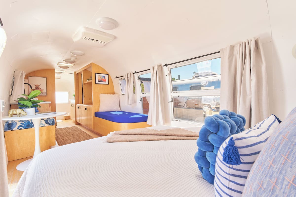 A cozy room with a bed, a small desk, a window with curtains, and a view of a boat outside.