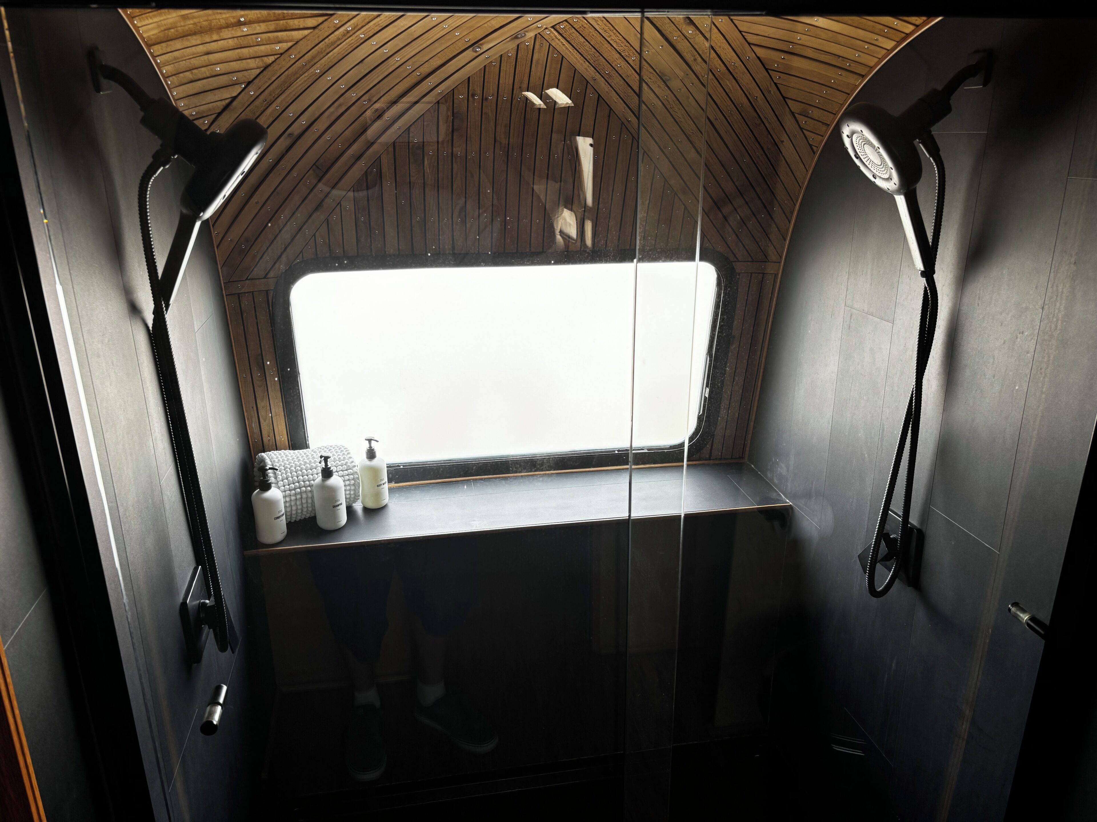 Un piccolo bagno con doccia chiuso, dotato di finestra, porta asciugamani e articoli da toilette.