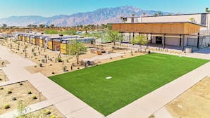 A modern hotel with a central courtyard, outdoor seating, and a mountain backdrop. - Acres Landing (Desert Hot Springs)