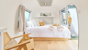 A bedroom with a bed, a bedside table, a chair, and a window. - Acres Landing (Desert Hot Springs)