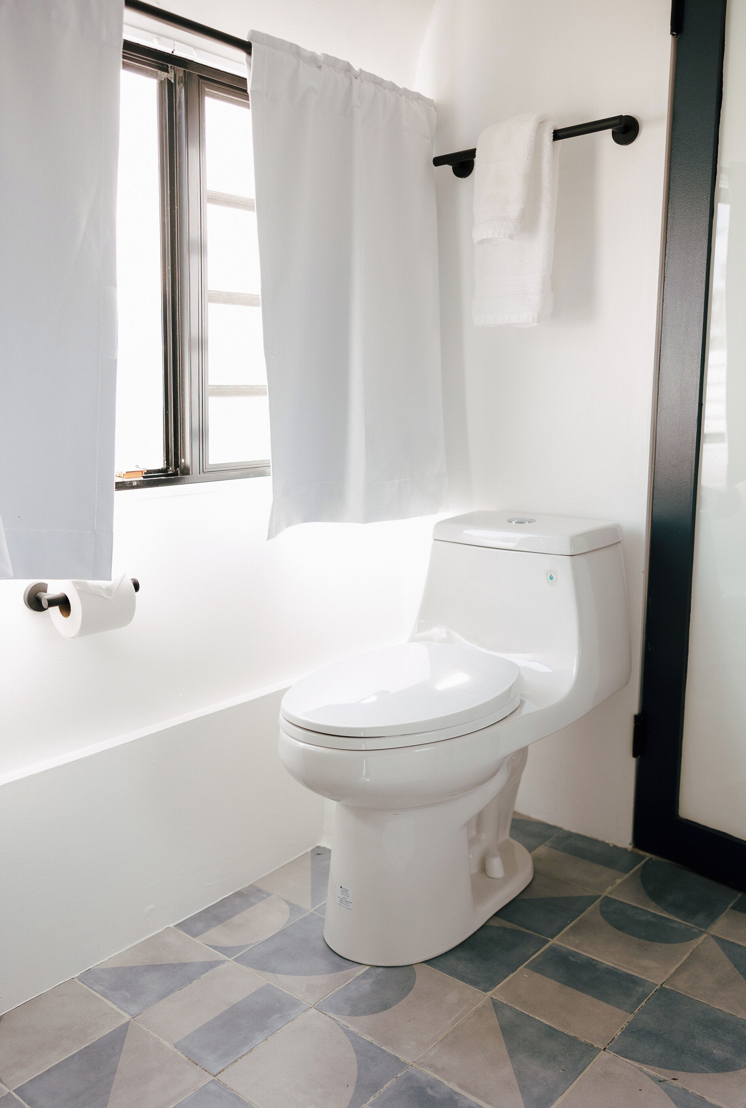 A bathroom with a toilet, a bathtub, and a window with curtains.
