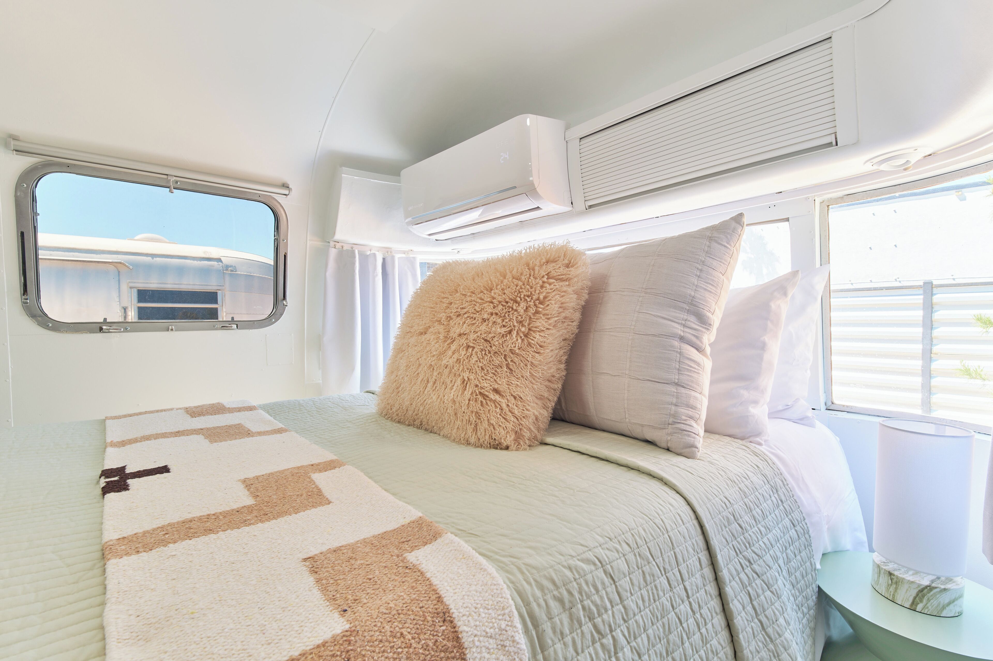 A bedroom with a bed, pillows, a window, and an air conditioning unit.