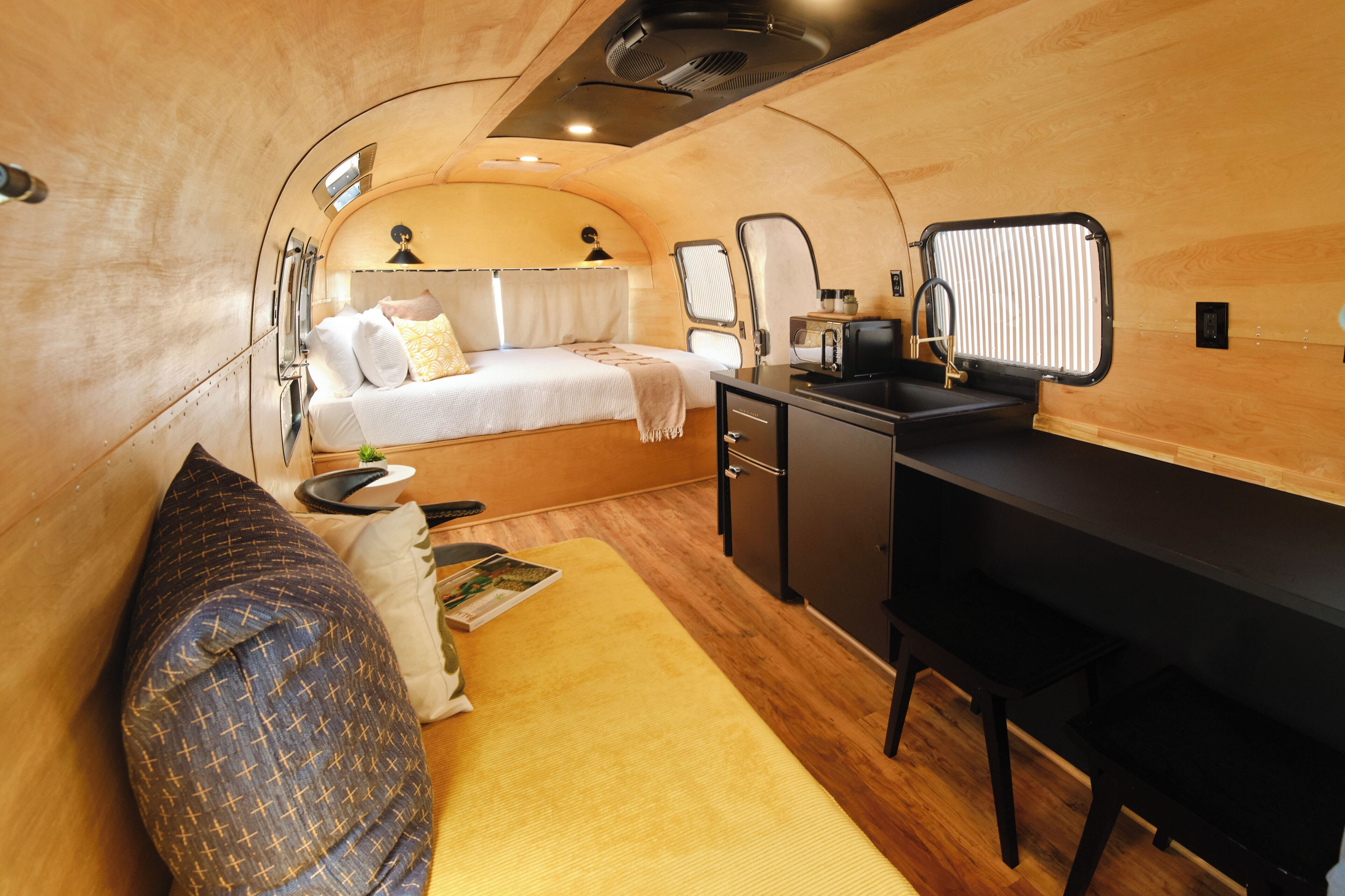 A compact, well-lit interior with a bed, a small kitchenette, and a desk area.