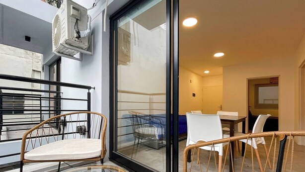 Une chambre d’hôtel moderne dotée d’une porte vitrée donnant sur un balcon, aménagé avec des fauteuils en osier et une petite table.