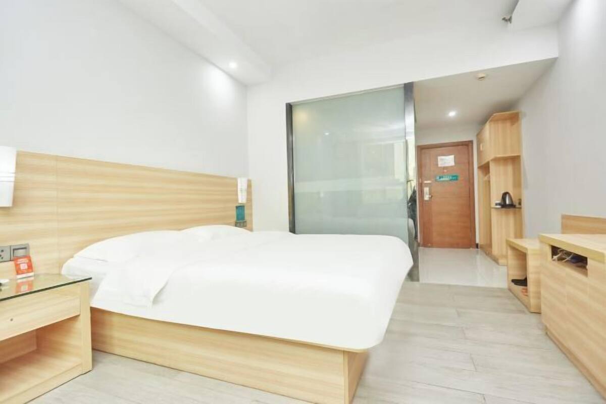 Ein modernes Hotelzimmer mit einem hölzernen Bett, einer Glastrennwand, einem Schreibtisch aus Holz und einer kleinen Sitzecke.