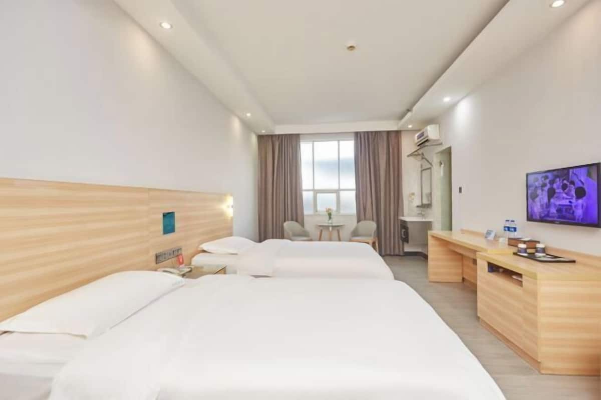 Ein Hotelzimmer mit zwei Betten, einem Schreibtisch, einem Fernseher und einem Fenster mit Vorhängen.