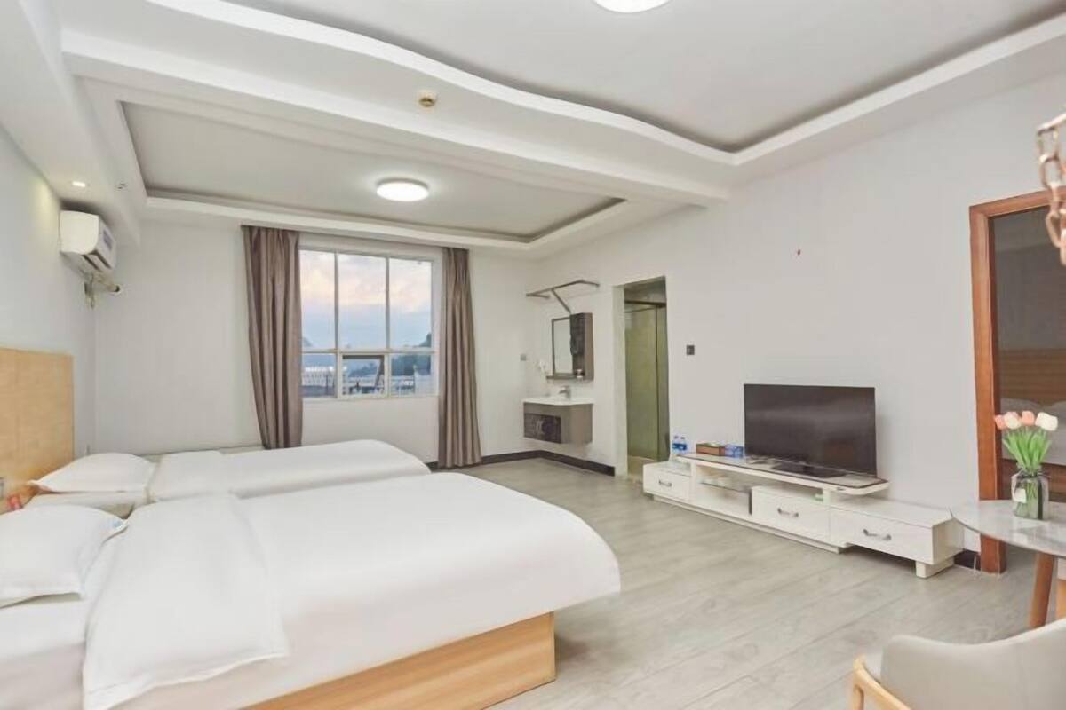 Ein Hotelzimmer mit zwei Betten, einem Fernseher, einem kleinen Tisch und einem Fenster mit Vorhängen.