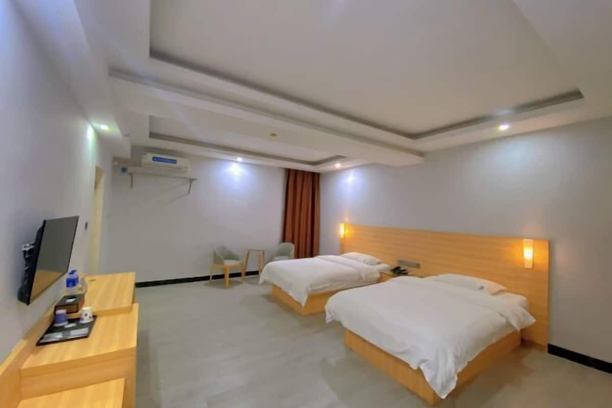 Ein Hotelzimmer mit zwei Betten, einem Schreibtisch, einem Sessel, einem Fernseher und einer Decken-Klimaanlage.