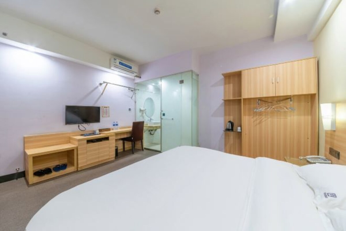 A hotel room with a bed, a desk, a chair, a TV, a wardrobe, and a mirror.