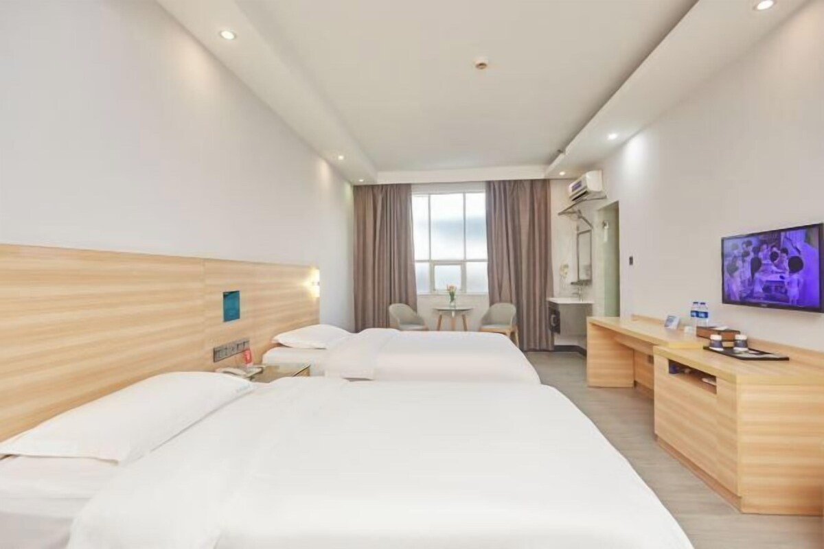Habitación de hotel con dos camas, un escritorio, un televisor y una ventana con cortinas.