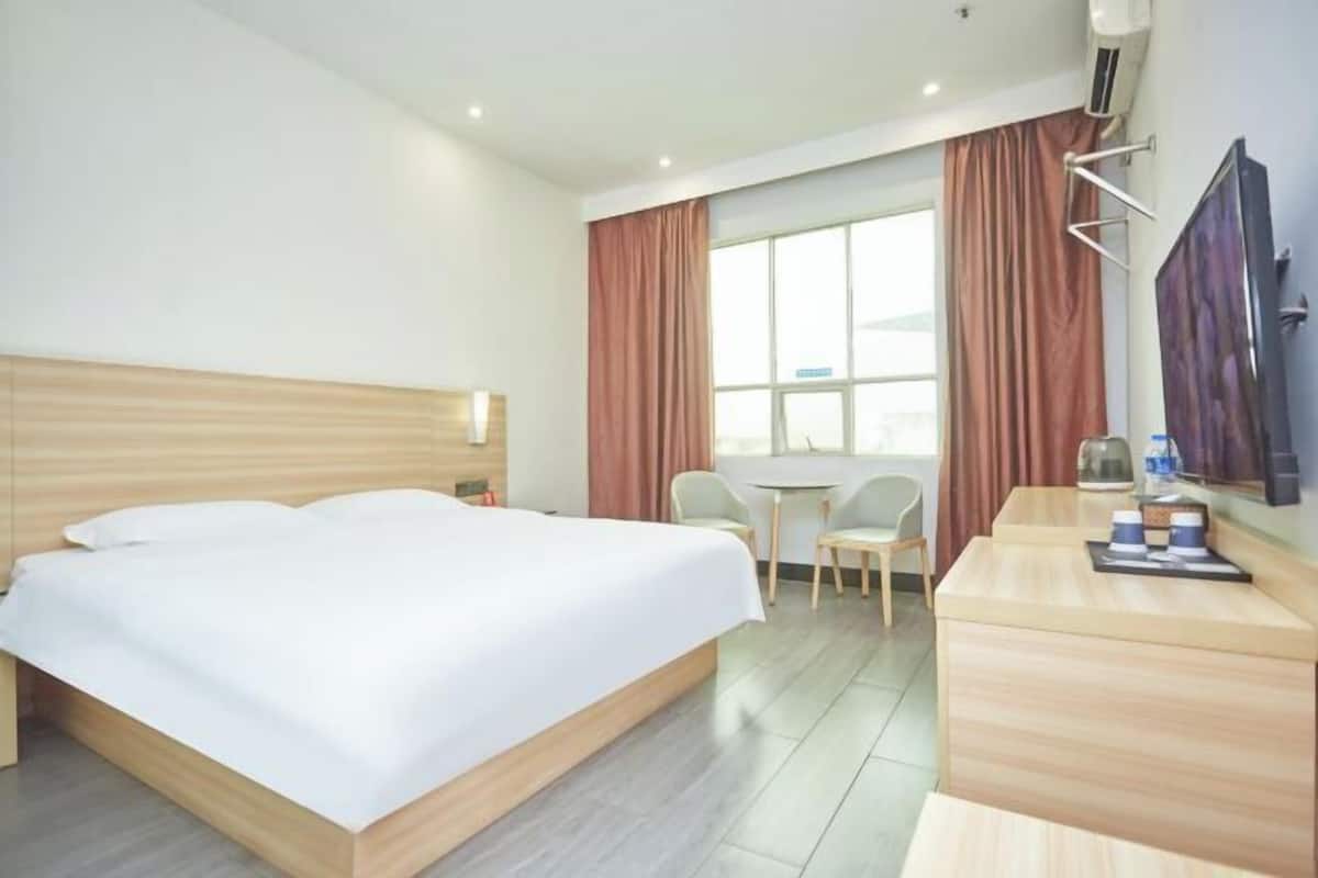 Ein Hotelzimmer mit Bett, Schreibtisch, Stuhl, einem Fenster mit Vorhängen und einem Flachbildfernseher.