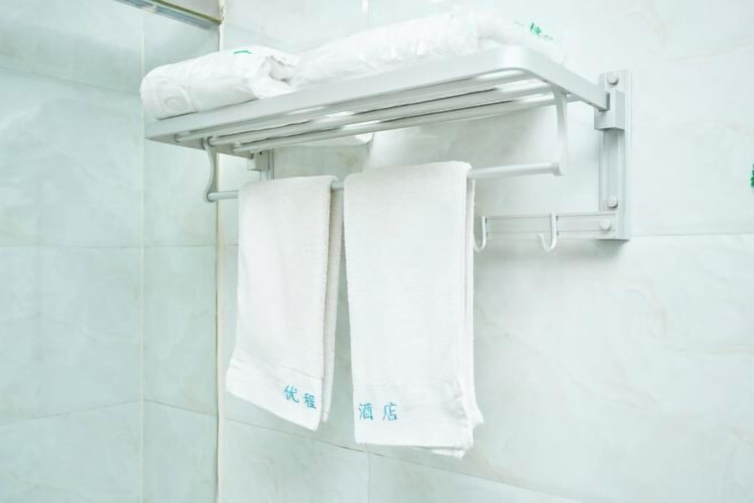 A bathroom with a towel rack holding two white towels and a folded towel on a shelf.