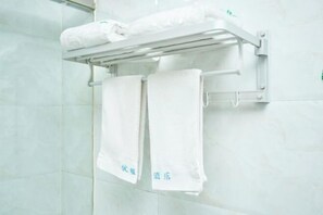 Un baño con un perchero que sostiene dos toallas blancas y una toalla doblada sobre una repisa.