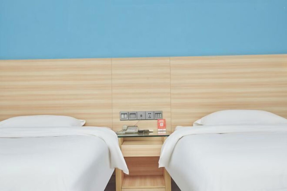 Habitación de hotel con dos camas, cabecero de madera, una mesita con un objeto rojo y un enchufe en la pared.