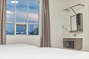 A hotel room with a large window, a bed, a bathroom with a mirror and sink, and a view of the mountains. - Balihotel (Wuxuan)
