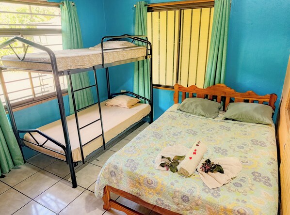 Cozy room with a bunk bed and single bed, featuring a window with green curtains and a floral-patterned bedspread.