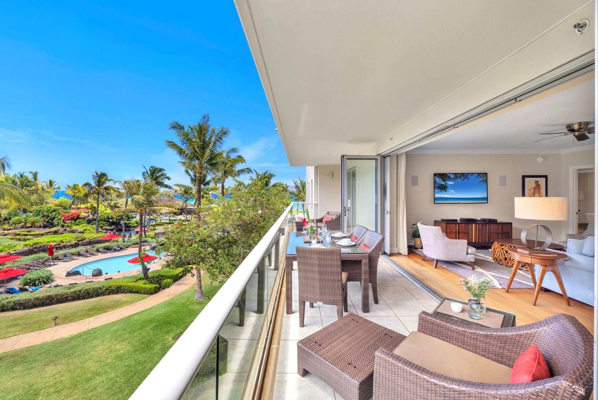 Un balcón con mobiliario de mimbre, una mesa de comedor y vistas a una piscina y un paisaje tropical.