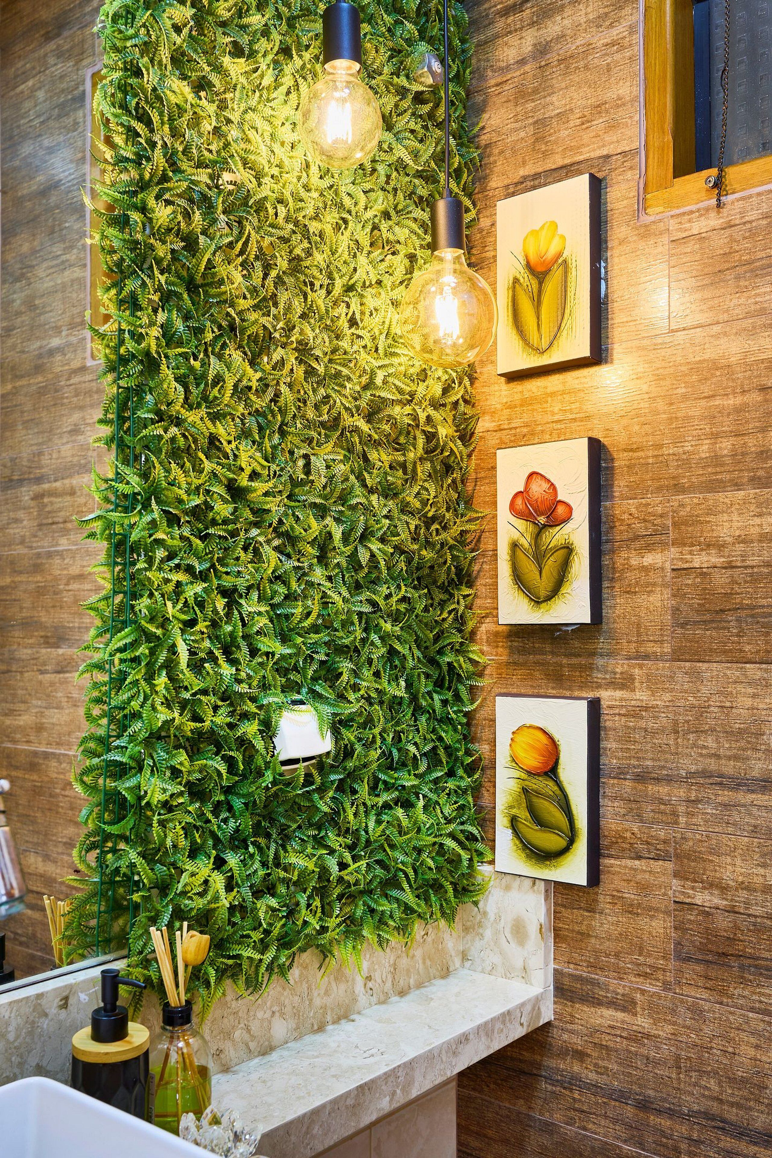 Una pared con jardín vertical, un espejo y tres ilustraciones botánicas enmarcadas.