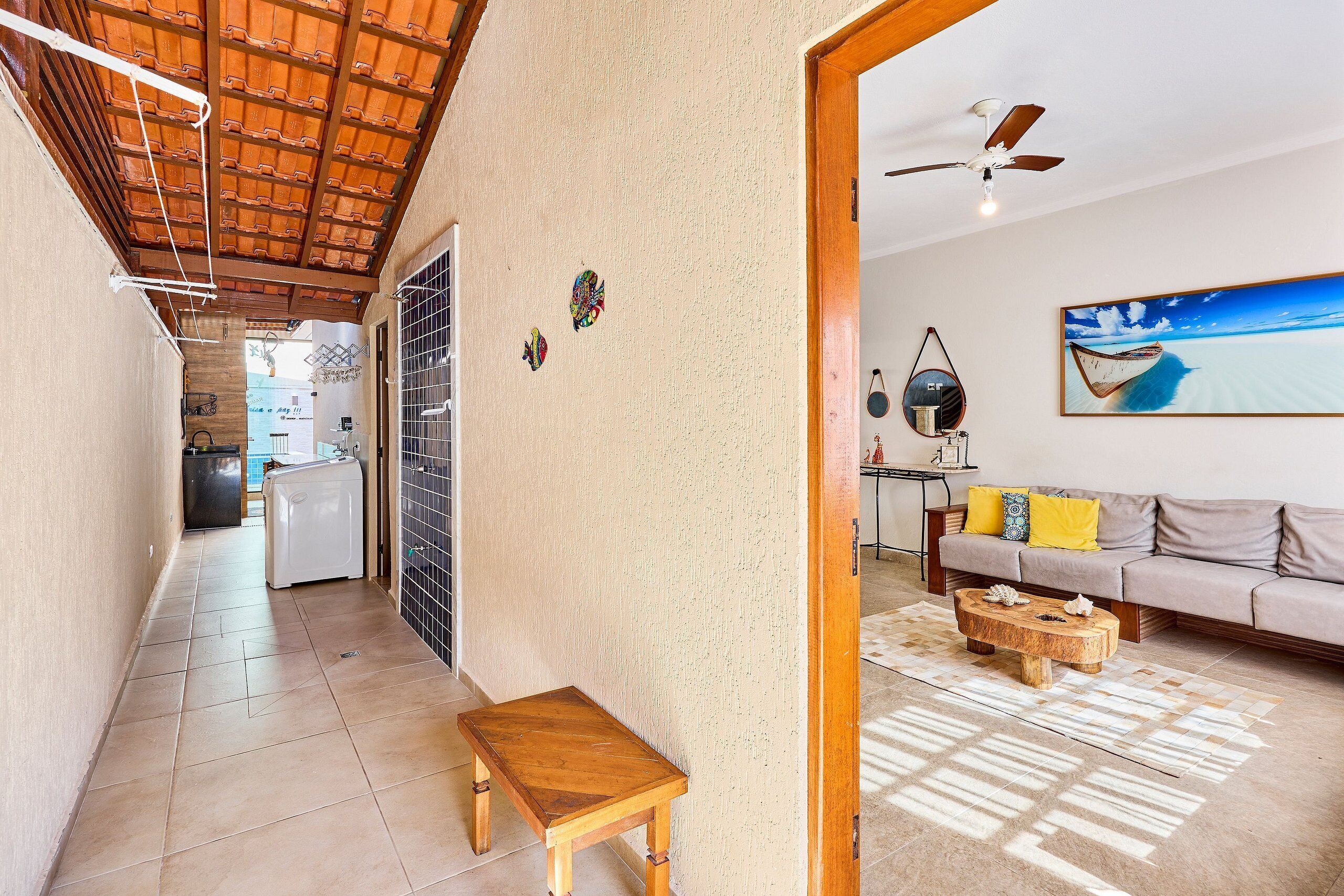 A hallway with a ceiling fan, a wooden bench, a refrigerator, and a dining area with a sofa and a table.