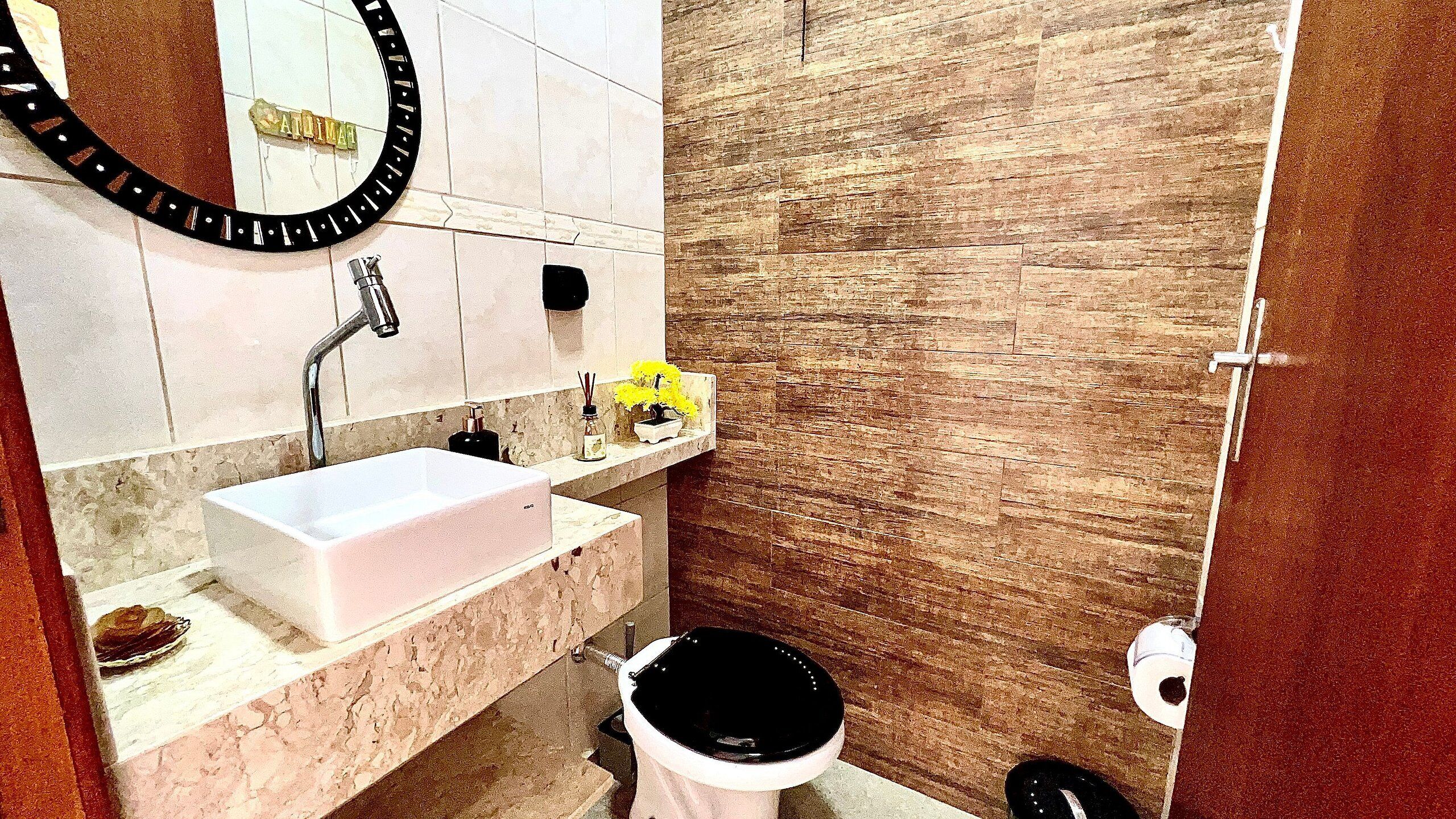 A bathroom with a white sink, a mirror with a black frame, a wooden wall, and a toilet.
