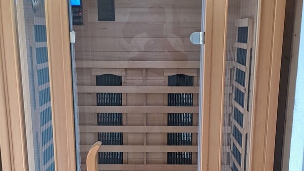 Una sauna con interni in legno, porte in vetro e una panca all'interno.