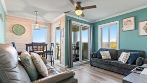 A living room with a leather sofa, a dark-colored couch, a ceiling fan, and a dining area with a table and chairs. - ONE More Sandy Day - 2BR/2BA Beach Condo, Sleeps 6 (Myrtle Beach)