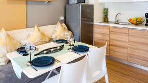 A modern kitchen with white cabinets, a microwave, and a refrigerator. There is a dining area with a table set for two, featuring blue plates and a glass.