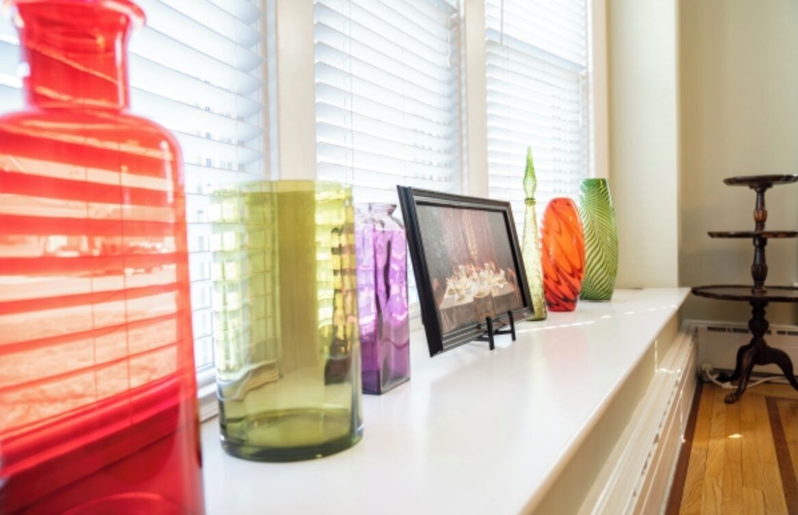 Un rebord de fenêtre orné de différents vases en verre et d’une photographie encadrée.