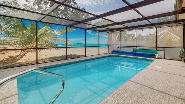 Una piscina interna con vista su una spiaggia e palme attraverso ampie finestre.