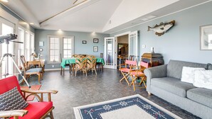 Un salón amplio con un sofá gris, sillas rojas y de madera, una zona de comedor con una mesa verde y un ventilador de techo.