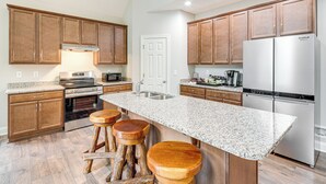 Una cocina con armarios de madera, un refrigerador de acero inoxidable, encimeras de granito y un horno empotrado.