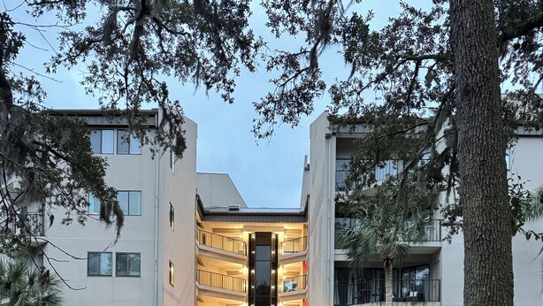 A building with a central entrance, surrounded by trees and a small pond. - Exceptional location!  Across the street from the beach! Walk to Everything!  (Hilton Head Island)