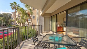 A balcony with a glass table and chairs, overlooking a street with palm trees and a red car. - Exceptional location!  Across the street from the beach! Walk to Everything!  (Hilton Head Island)