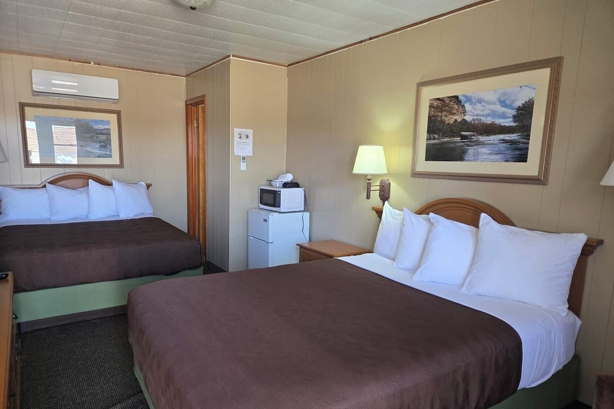 Ein Hotelzimmer mit zwei Betten, einer Mikrowelle, einem kleinen Schreibtisch und einem Bild an der Wand.