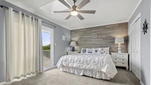 Quarto com cama, mesas de cabeceira, ventoinha no teto e vista por uma porta de correr.
