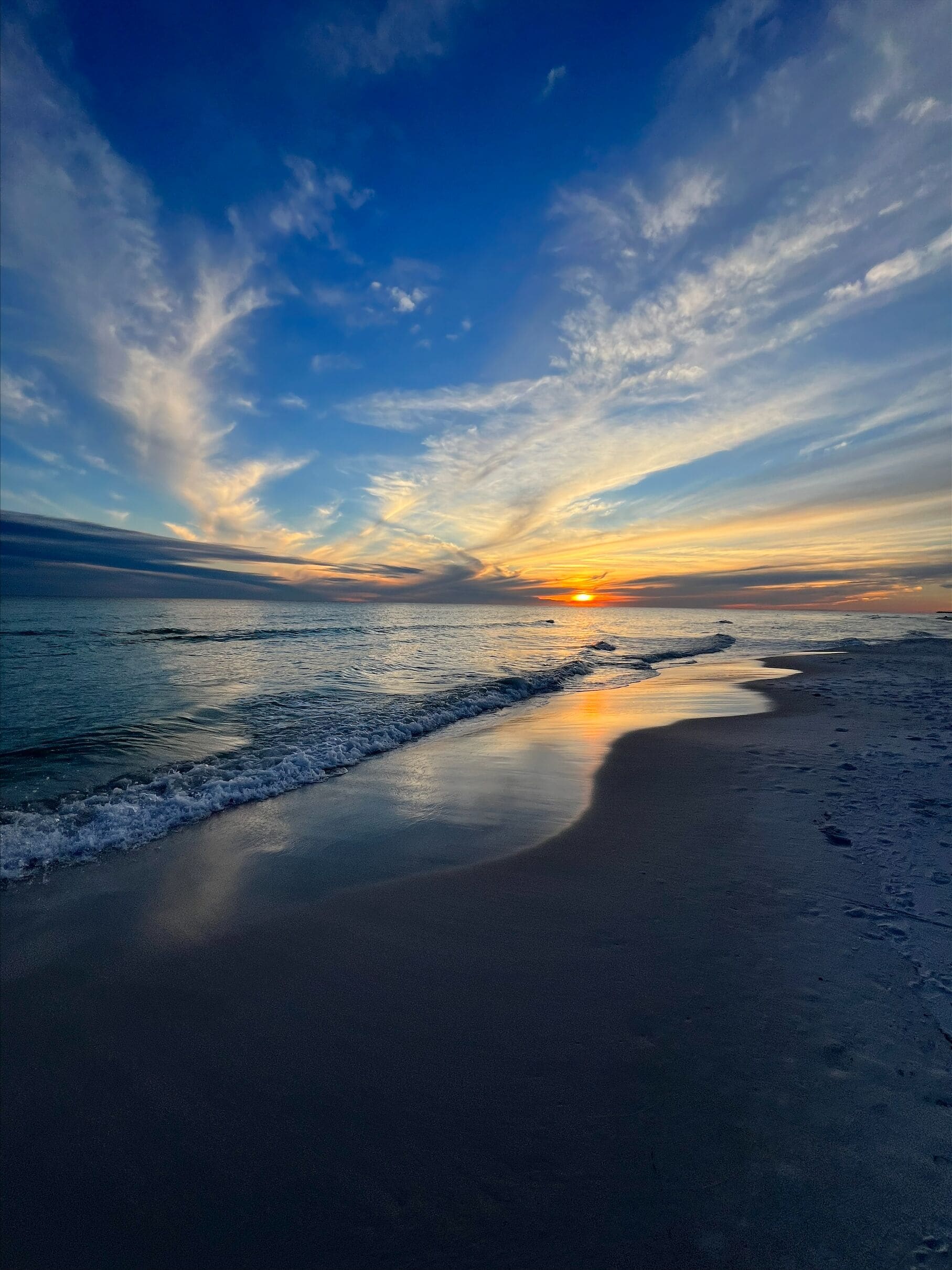 A beach with a sunset, waves, and a clear sky.