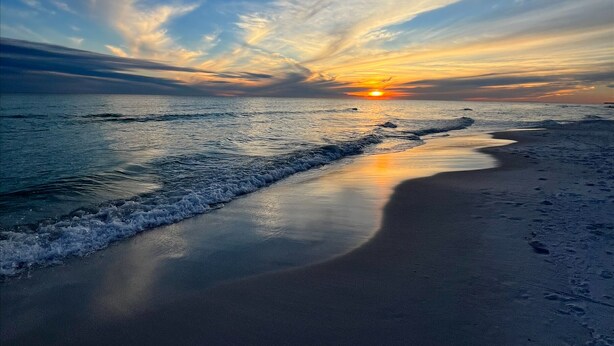Uma praia com um pôr do sol, ondas e céu claro.