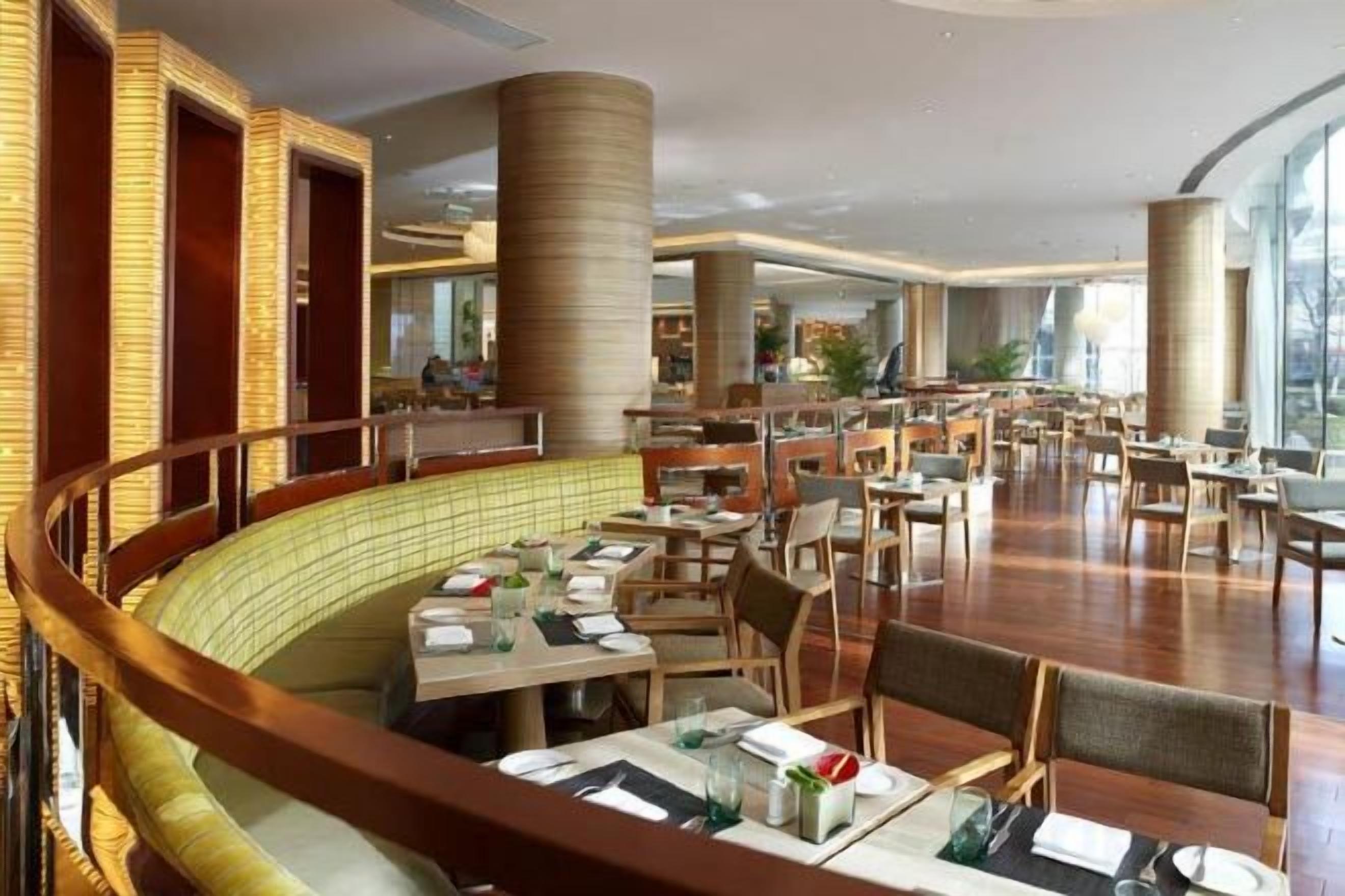 Um restaurante amplo com várias áreas de refeições, pé direito alto e grandes janelas.