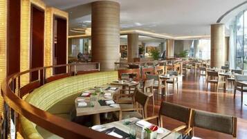 Um restaurante amplo com várias áreas de refeições, pé direito alto e grandes janelas.