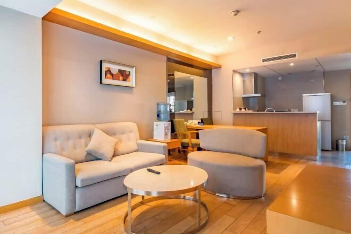 A modern living room with a sofa, armchair, and coffee table, a kitchen area with a refrigerator and stove, and a dining area with chairs.