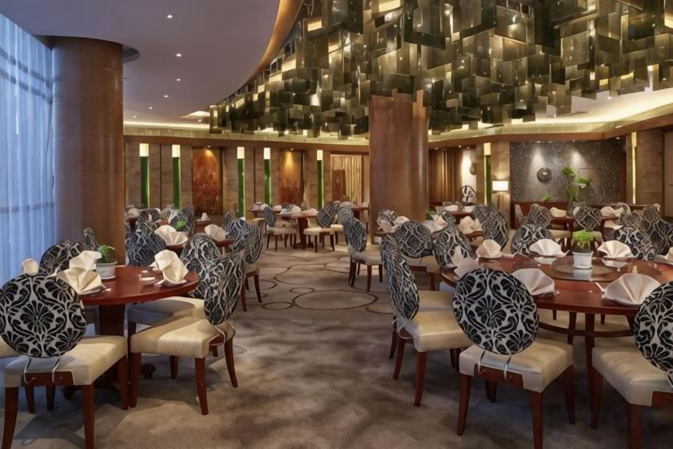 A spacious hotel dining area with round tables and chairs, a high ceiling, and a modern design.