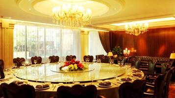 A round table with chairs, a chandelier, and a dining setup in a room with large windows and curtains.
