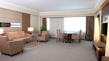 A hotel room with a sofa set, a dining table with chairs, a TV, and a large window with curtains.