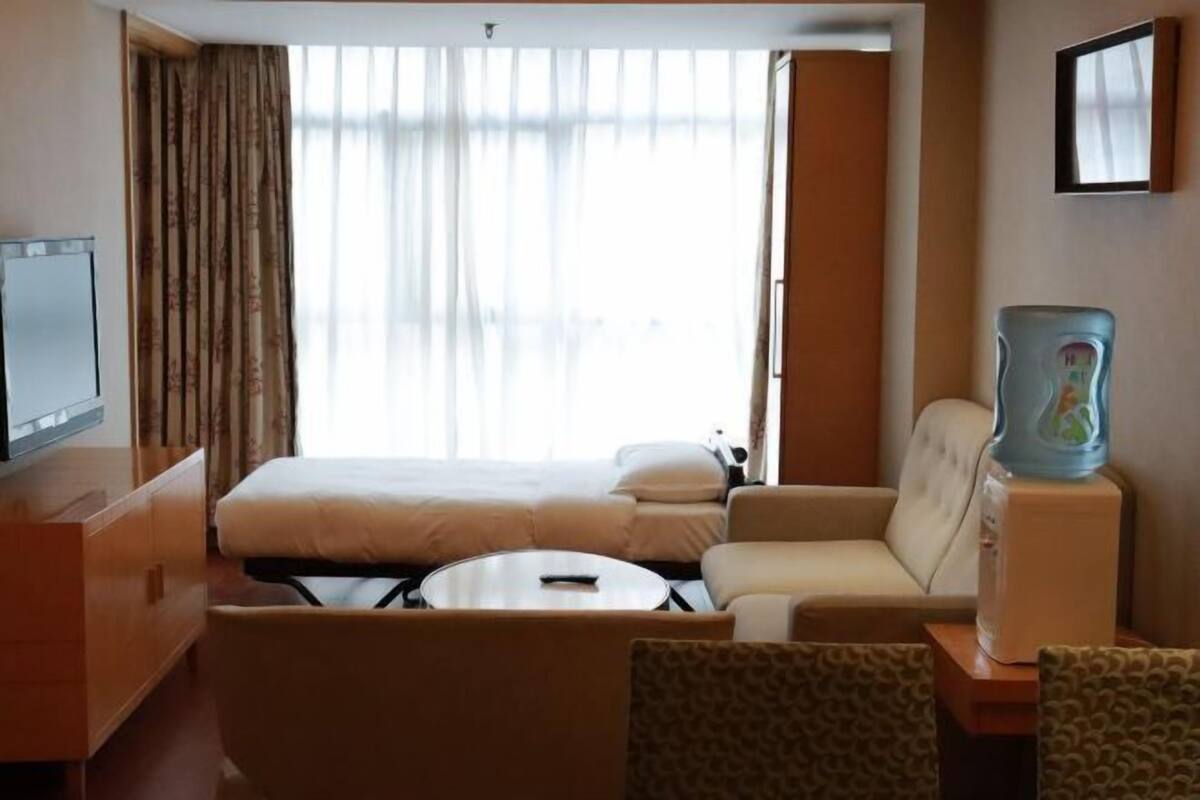 A hotel room with a bed, a sofa, a small table, a television, and a water dispenser.